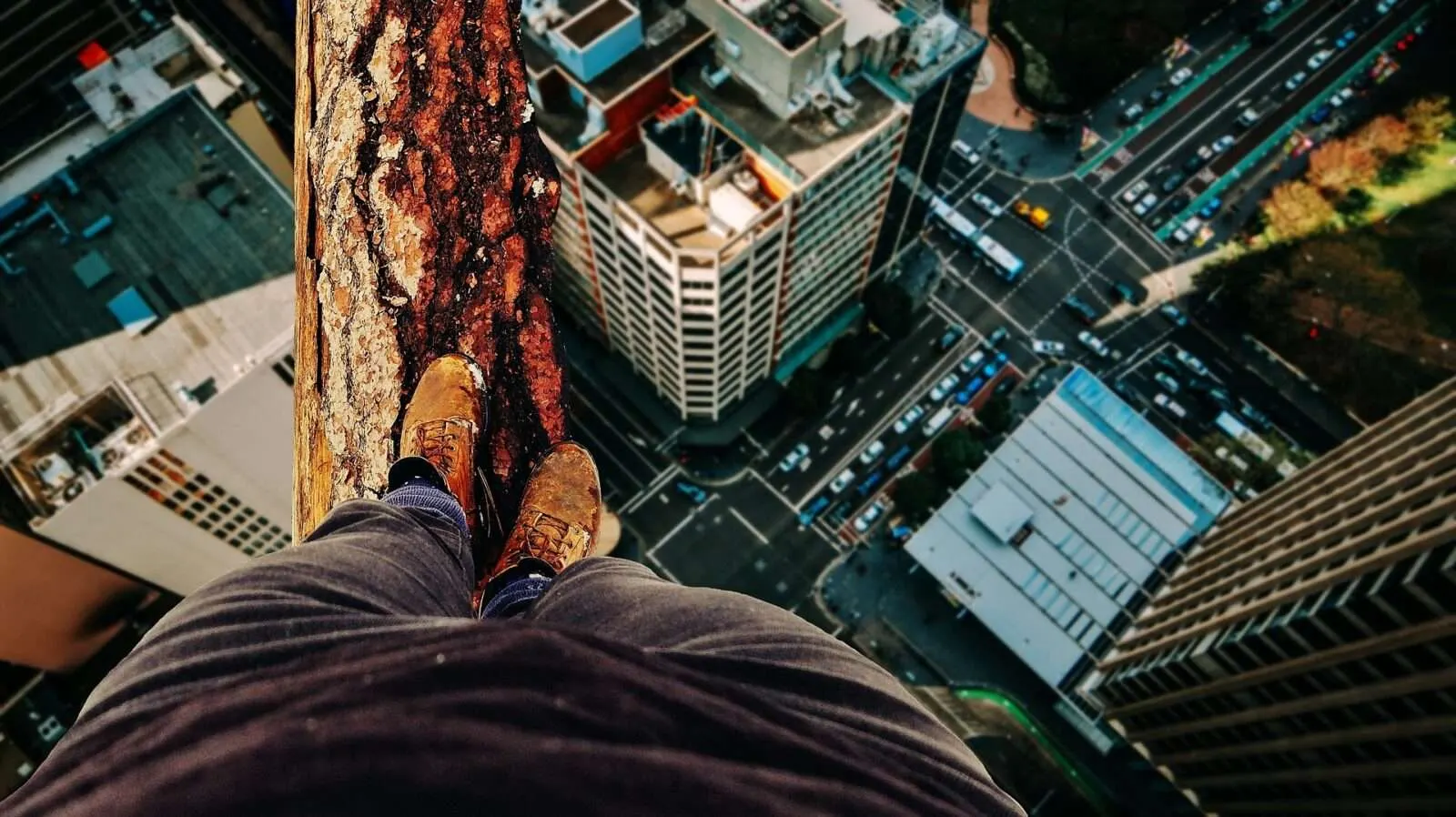 Eine Person balanciert in schwindelerregender Höhe über einer Großstadt auf einem Holzbalken mit Blick in die Tiefe. Gefahren richtig einschätzen, Umgang mit Gefahren, objektive und subjektive Gefahren, Mentaltraining, Mind Set