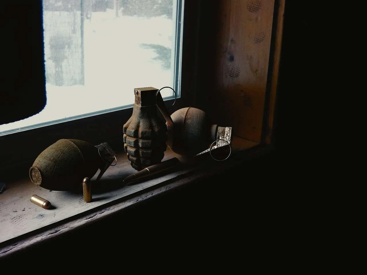Verschiedene Handgranaten und Patronen auf einer Fensterbank in einem Kriegsgebiet Bosniens der 1990er