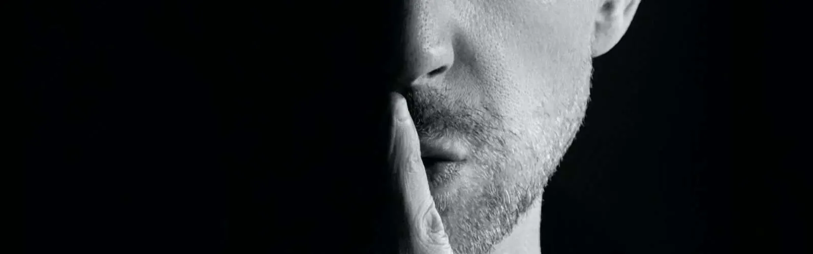 Ein Mann, der seinen Zeigefinger vor die Lippen hält, um Stille zu signalisieren