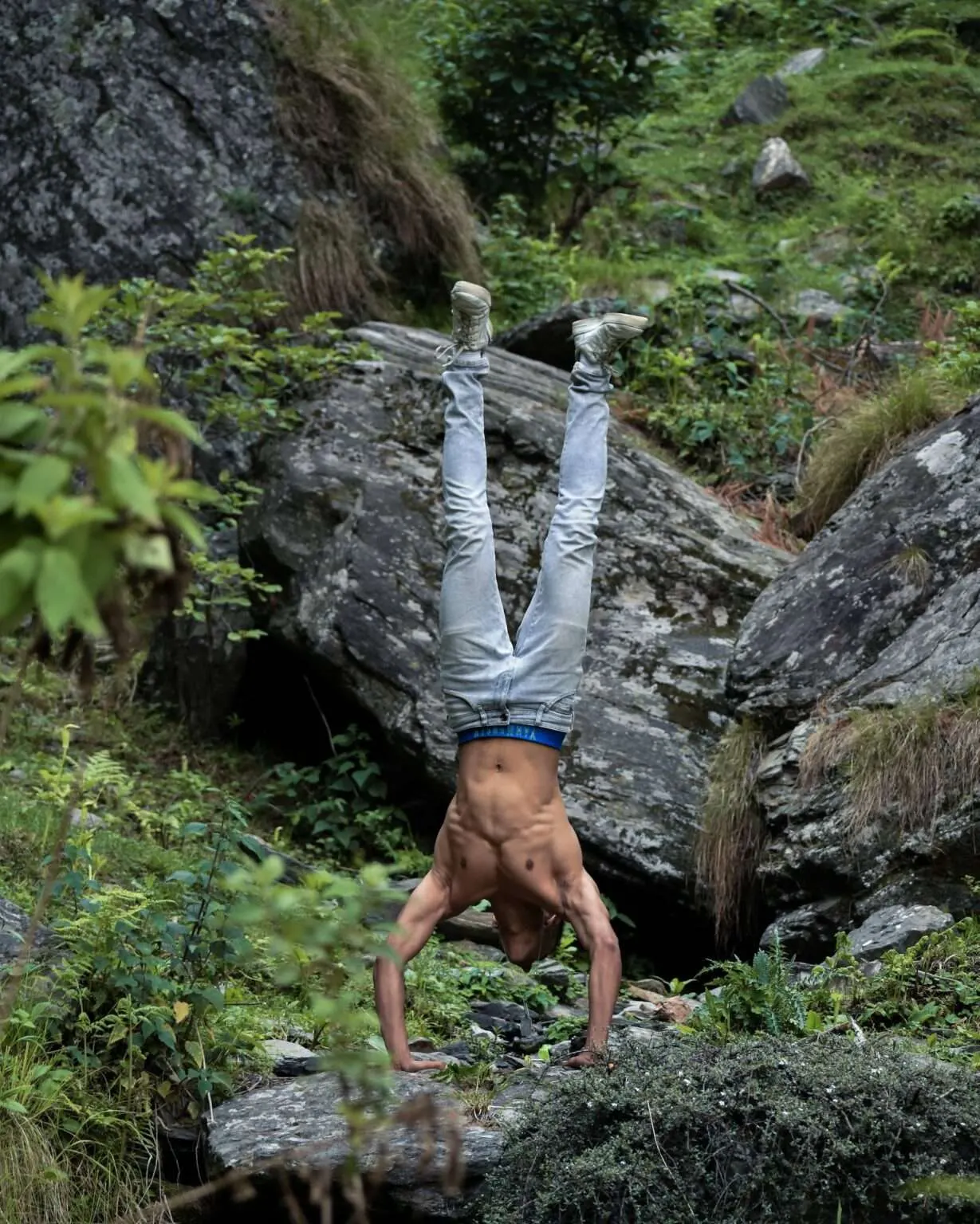 Ein Mann in der Wildnis, der oberkörperfrei einen Handstand auf zwei Steinen macht