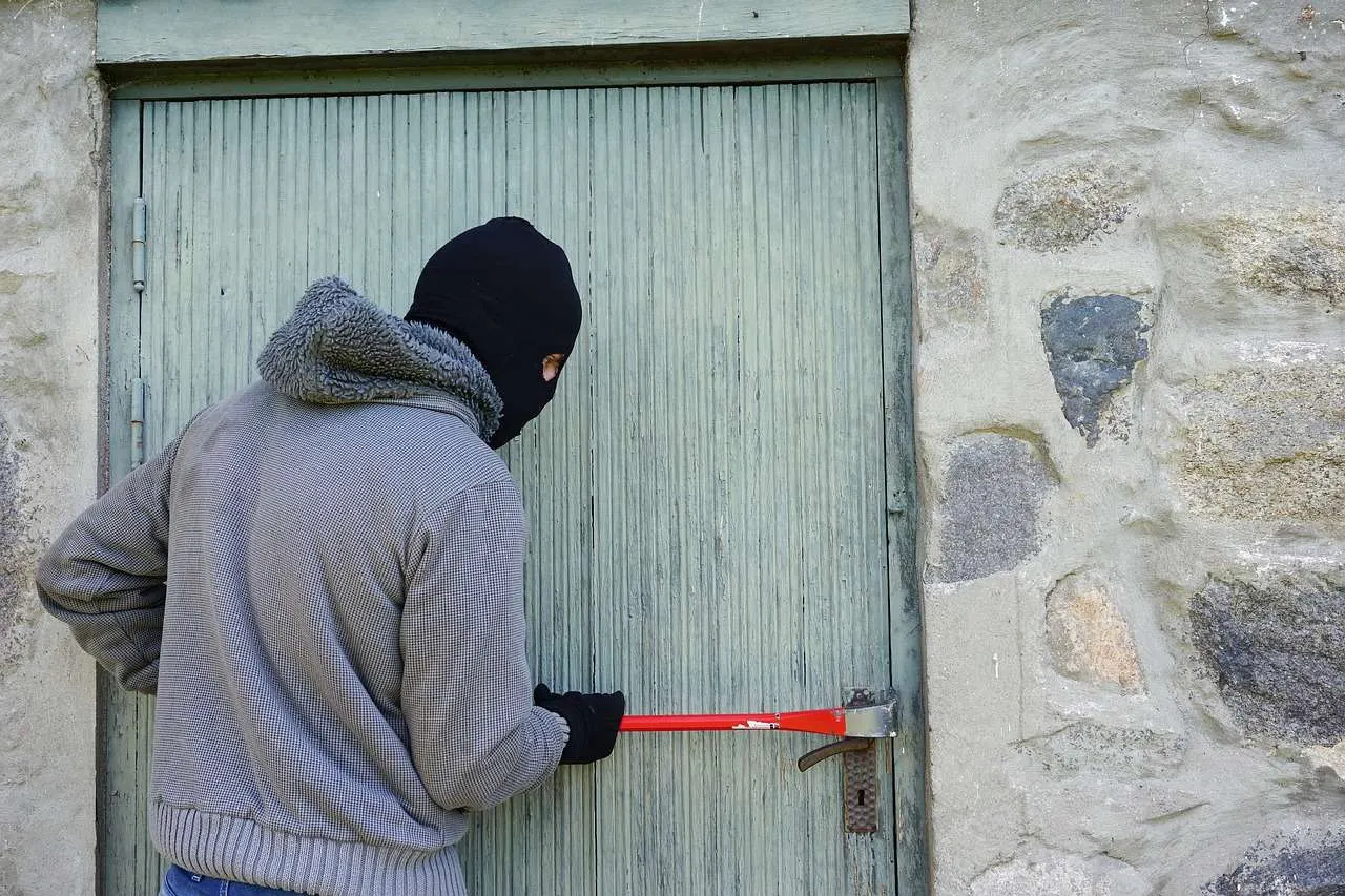 Ein maskierter Einbrecher, der mit einer Brechstange an einer verschlossenen Holztür versucht einzubrechen